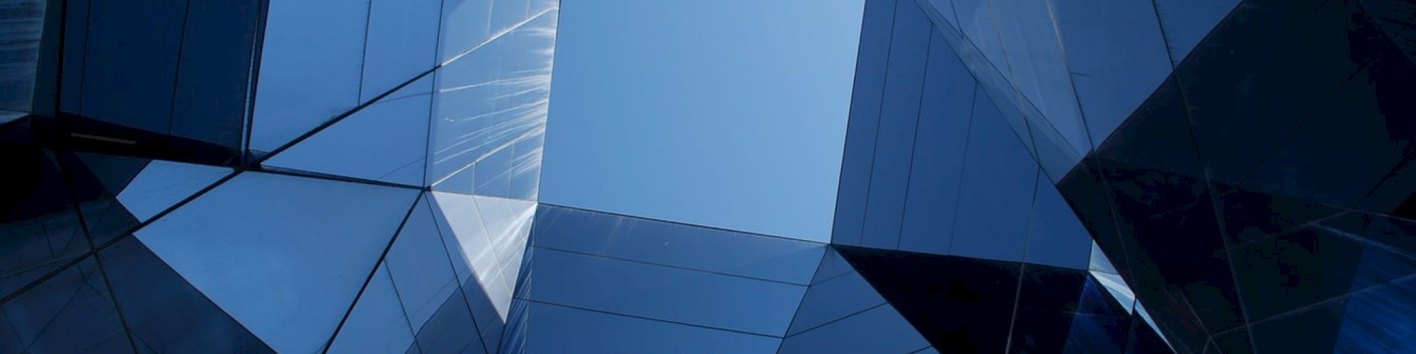 The image depicts a geometric pattern formed by modern glass buildings, with the sky visible through an opening at the center of the composition.
