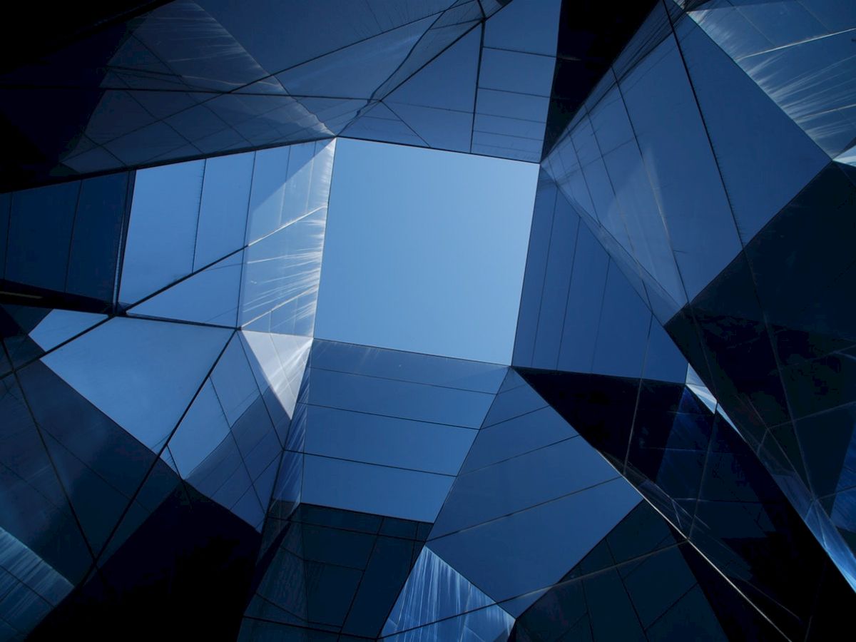 The image shows a geometric arrangement of reflective glass structures forming a hexagonal pattern, with the sky visible through the center opening.