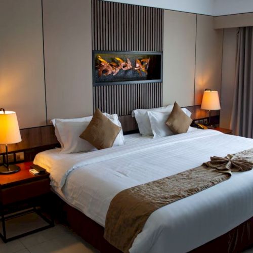 A neatly made bed in a hotel room, flanked by two bedside tables with lamps, and a wall decoration above the headboard.
