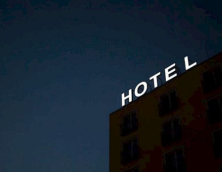A building with a large neon sign that says "HOTEL" is shown at night, with the sky being dark and the building illuminated.
