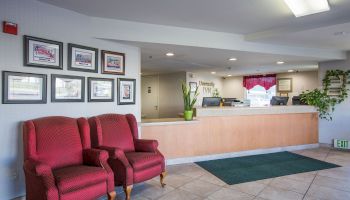 The image shows a hotel lobby with two red armchairs, framed pictures on the wall, a reception desk, and tile flooring.