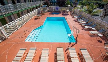 This image shows an outdoor pool area with several lounge chairs and tables around it, and a fence enclosing the space.