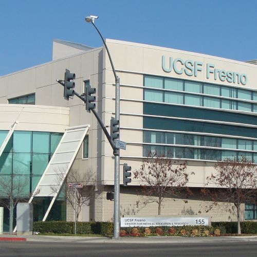 The image shows the exterior of the UCSF Fresno building with modern architectural design, including angled glass panels and a multi-story structure.