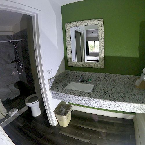 A bathroom with a green wall, a sink, a mirror, a toilet, a shower with a curtain, and neatly folded towels can be seen.