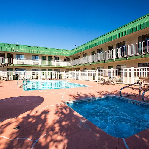 The image shows a hotel courtyard with a swimming pool and hot tub, surrounded by lounge chairs and a two-story building with green roofing.