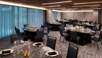 The image shows a banquet hall with round tables set for an event. Each table is neatly arranged with cutlery, glassware, and napkins.