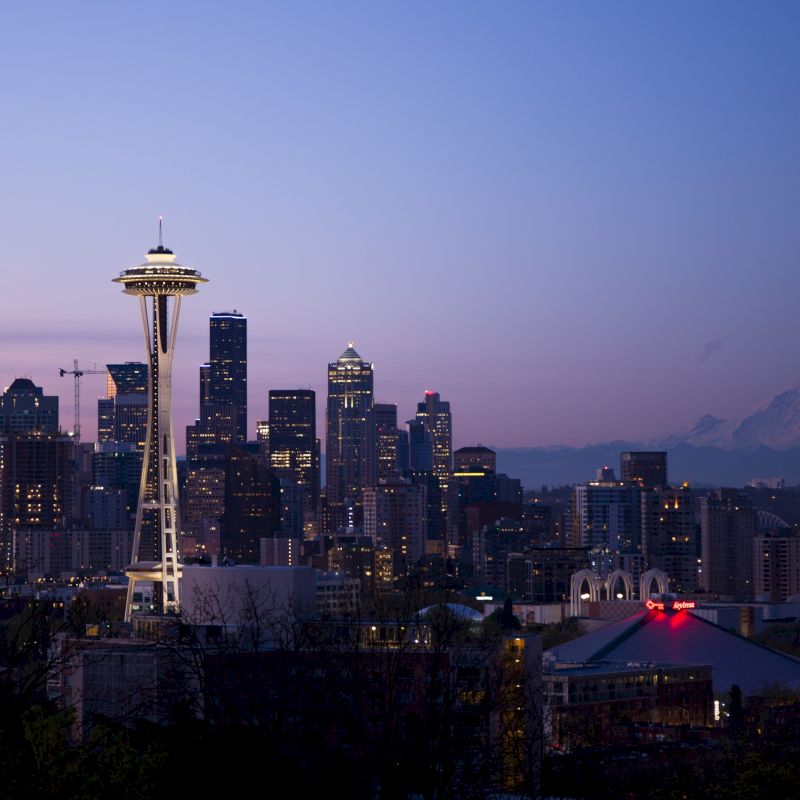 The image shows the Seattle skyline at dusk, featuring the Space Needle and various buildings, with Mount Rainier visible in the background.