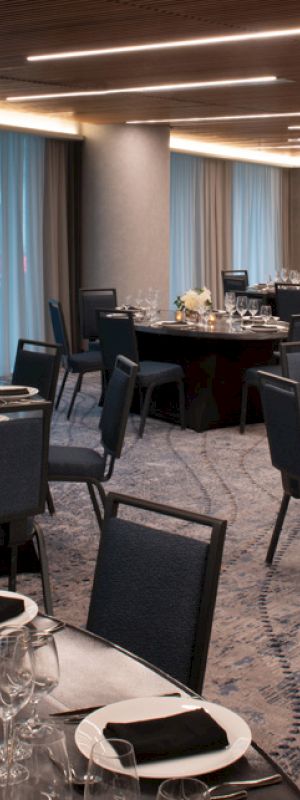 A banquet hall with multiple round tables is set for an event, featuring elegant table settings with black napkins and floral centerpieces.