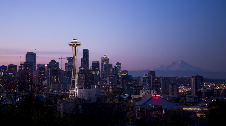 This image shows the Seattle skyline at dusk, featuring the Space Needle in the foreground and Mount Rainier in the background.