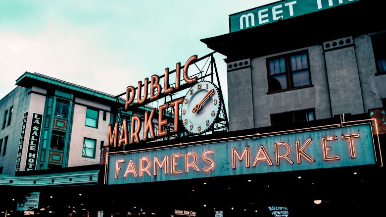 The image shows a public market building with neon signs that read "Public Market" and "Farmers Market", along with a clock at the center.
